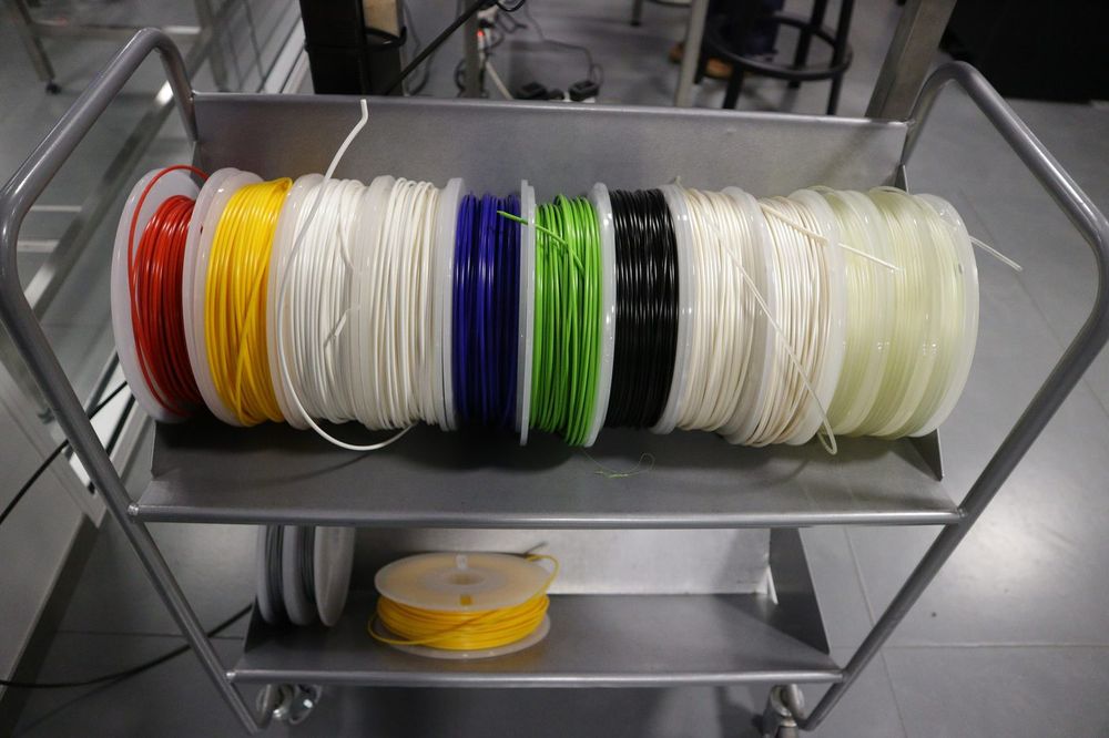 Carrinho metálico com carretéis de filamento para impressora 3D em vermelho, amarelo, branco, azul, verde e preto.
